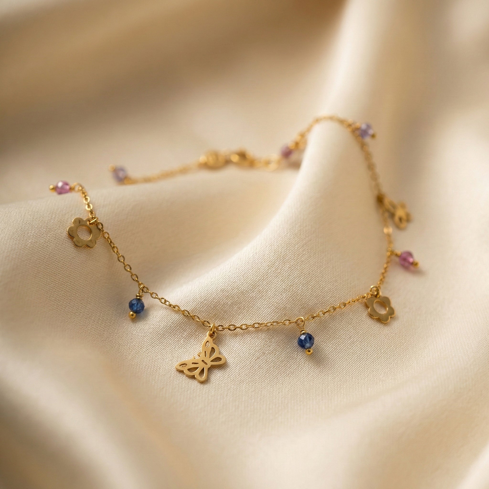 Gold anklet with butterfly charm and small beads on a beige fabric background