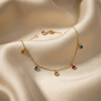 Gold anklet with colorful gemstones on a soft beige fabric background