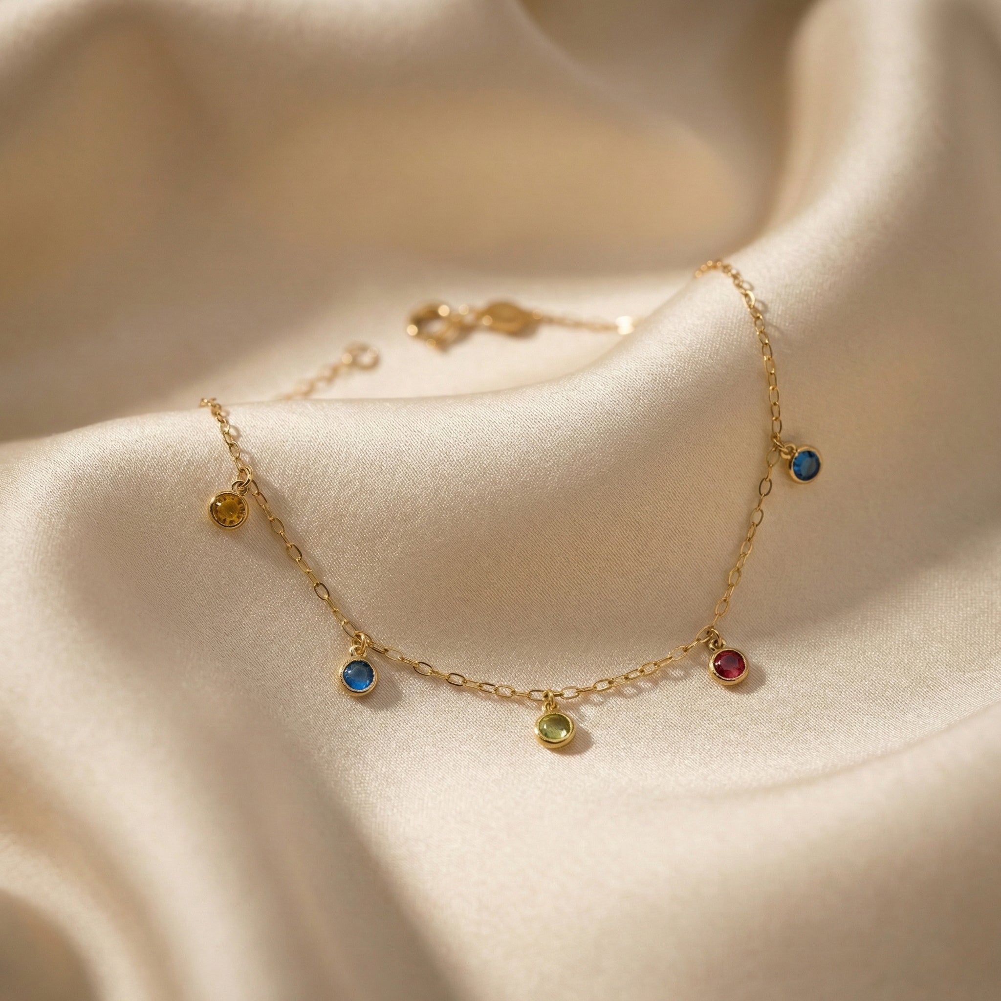 Gold anklet with colorful gemstones on a soft beige fabric background