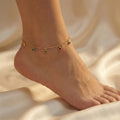 Gold anklet with colorful beads on a foot against a beige background