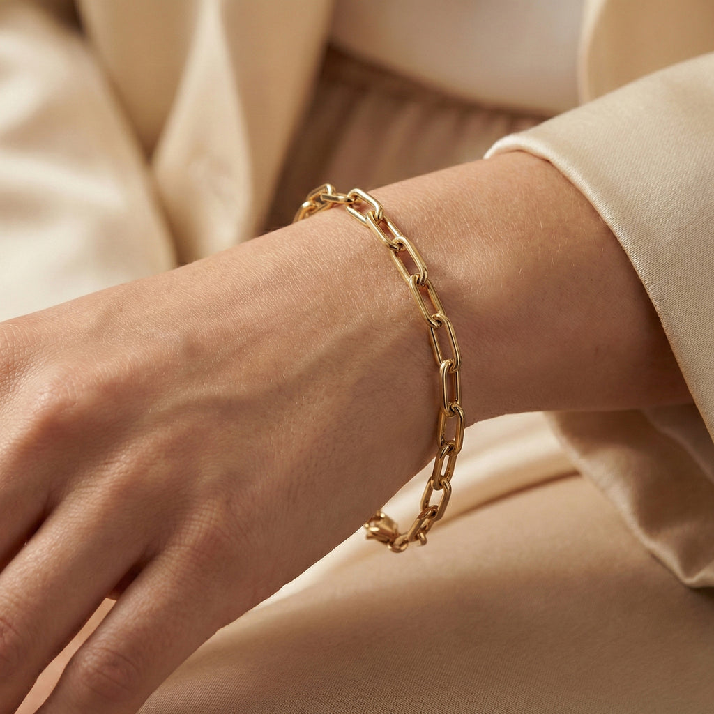 Gold chain bracelet on a wrist with a neutral background