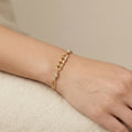 Gold chain bracelet on a wrist against a beige background