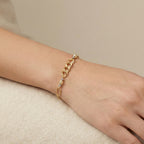 Gold chain bracelet on a wrist against a beige background