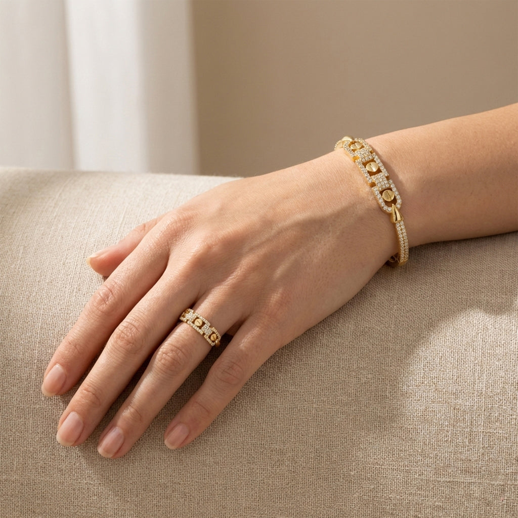 Hand wearing a gold ring and bracelet on a beige surface