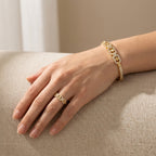 Hand wearing a gold ring and bracelet on a beige surface