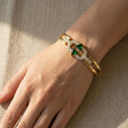 Gold bracelet with green gemstone on a wrist against a beige background