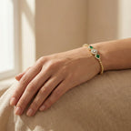 Gold bracelet with green gemstones on a hand resting on a beige surface