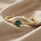 Gold bracelet with a green gemstone on a beige fabric background
