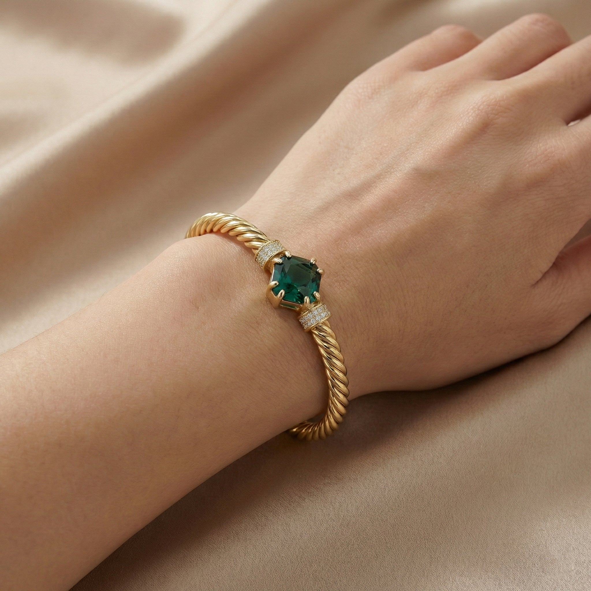 Gold bracelet with a green gemstone on a beige fabric background