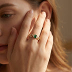 Close-up of a hand wearing a gold ring with a green gemstone, held near the face.