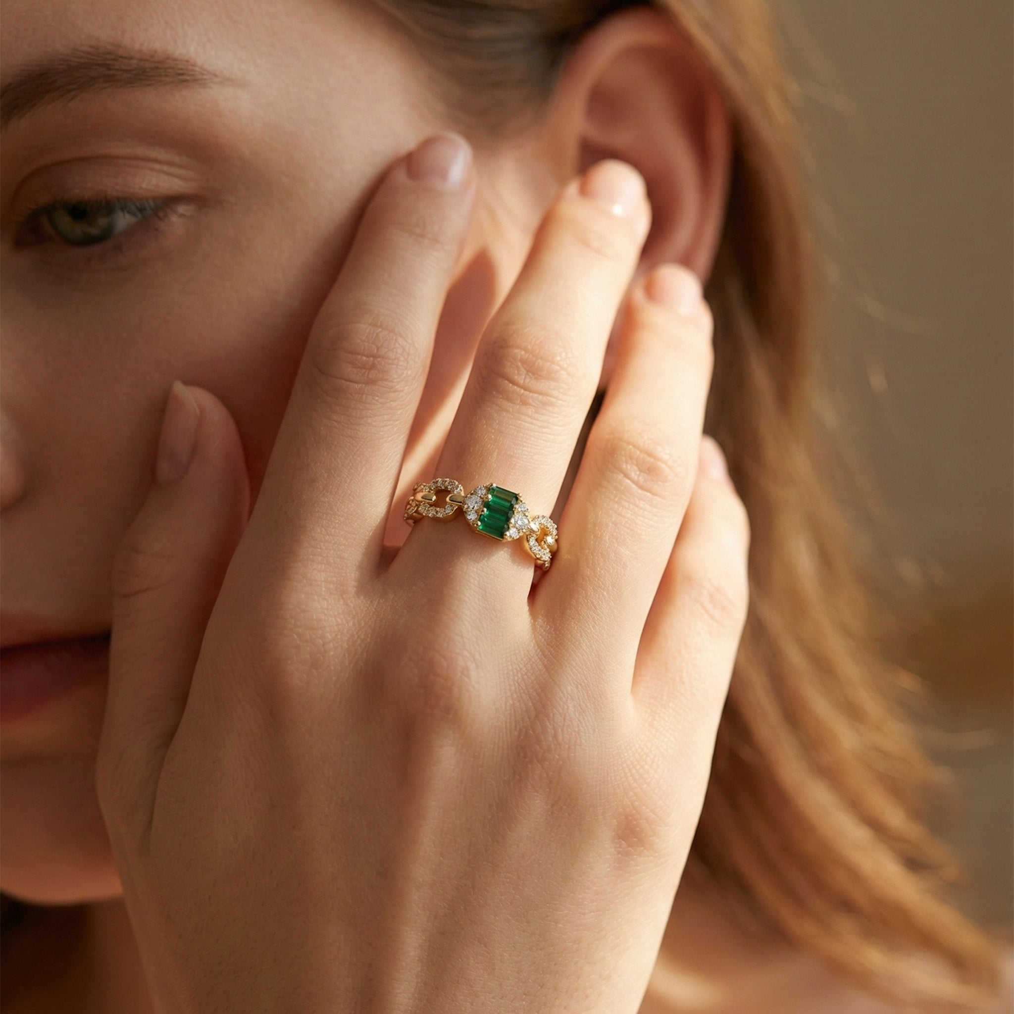 Close-up of a hand wearing a gold ring with a green gemstone, held near the face.