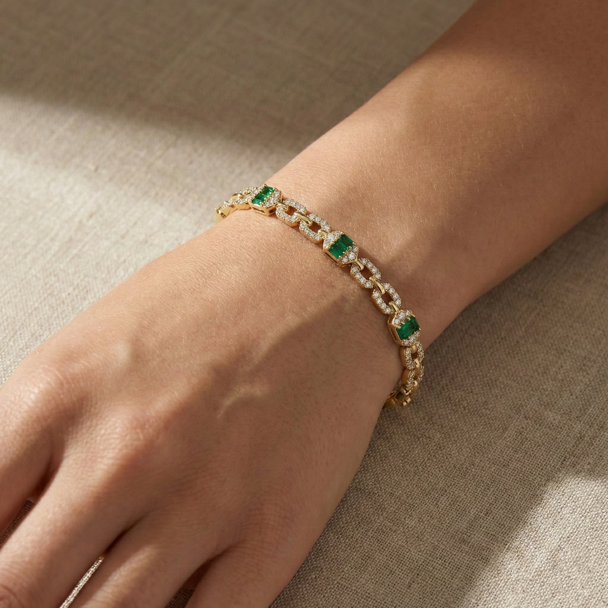 Gold bracelet with green gemstones on a wrist against a beige fabric background