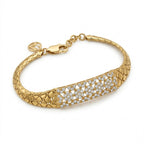 A Lazurde 18k yellow gold bracelet featuring a wide, woven-textured band and a central rectangular plate adorned with intricate floral pave-set stones, isolated on a seamless white background.