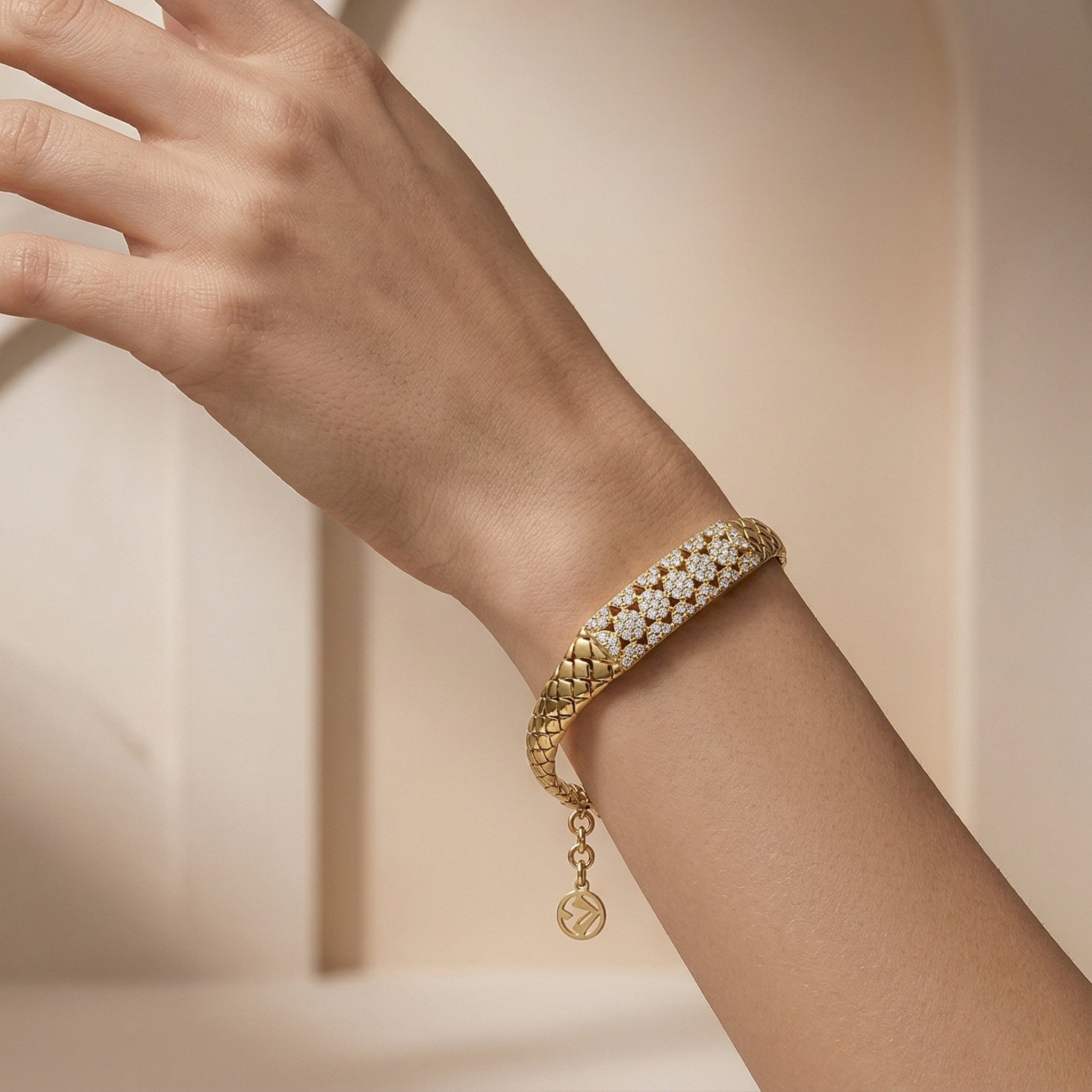 Editorial photograph of a Lazurde 18k yellow gold woven bracelet on a feminine wrist. The hand is posed sculpturally against a minimalist nude-beige background with soft architectural arches and delicate shadow play.