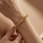 A warm, close-up lifestyle image of a person’s hands adjusting the Lazurde 18k yellow gold bracelet on their wrist. The shot highlights the detailed craftsmanship of the polished links and the brilliant shimmer of the stone-set charms.