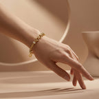 An elegant editorial shot of a woman’s hand reaching gracefully against a minimalist, nude-beige background. She is wearing the Lazurde 18k yellow gold bracelet, which stands out with its rich gold tones and intricate textures under soft, diffused lighting.