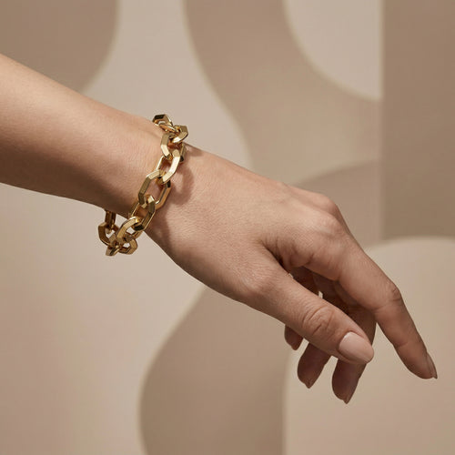Luxury editorial photo of a Dreams 18k yellow gold chunky chain bracelet on a feminine wrist, set against a minimalist nude-beige background with soft shadows.