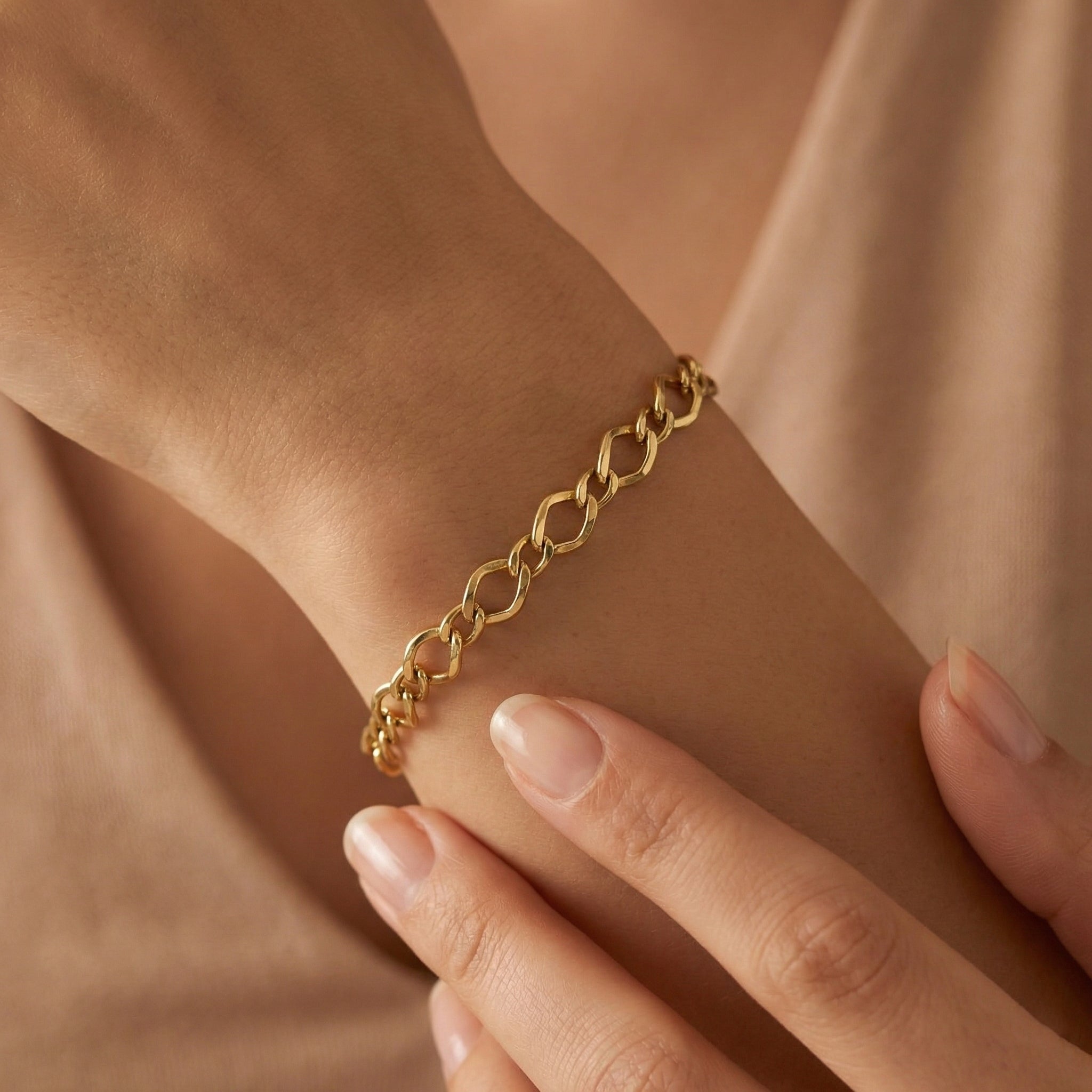 An ultra-realistic close-up of the 3B 18k yellow gold Gourmet bracelet worn on a feminine wrist, with the other hand gently touching it against a soft nude background in warm diffused lighting.