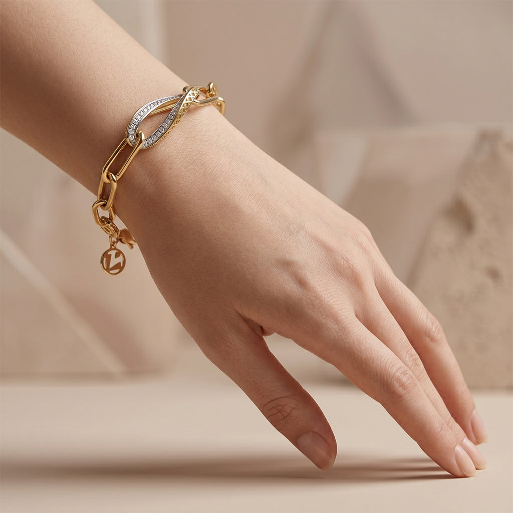 An elegant editorial photo of a Lazurde 18k yellow gold bracelet styled on a feminine wrist. The hand is posed sculpturally, resting lightly on a surface against a warm beige background with subtle abstract shapes, emphasizing the polished gold links and intricate center detail.