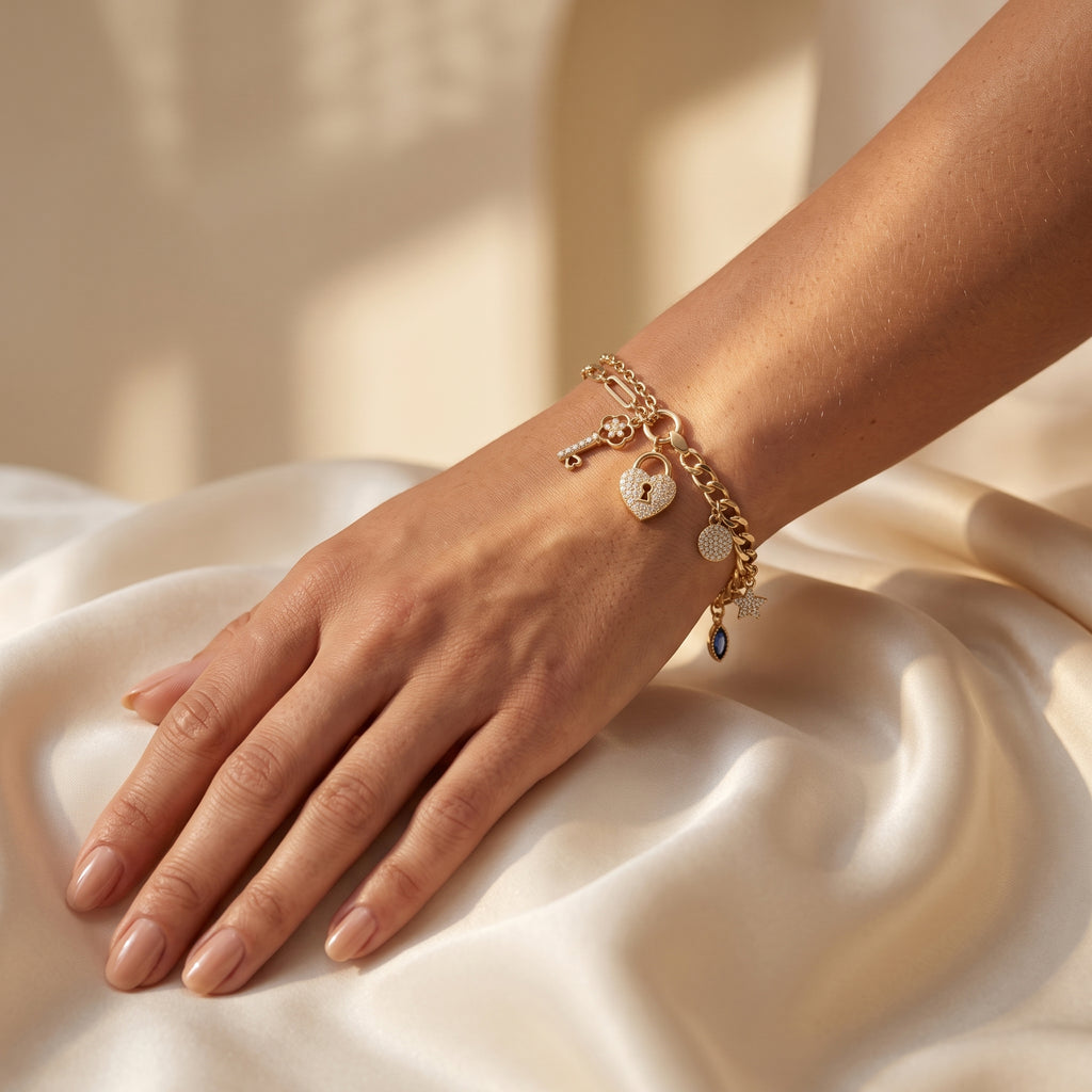Close-up of a L'azurde 18k yellow gold charm bracelet on a feminine wrist resting on elegant warm ivory silk fabric. صورة مقربة لسوار دلايات لازوردي ذهب أصفر عيار 18 على معصم أنثوي يستقر على قماش حرير عاجي فاخر.
