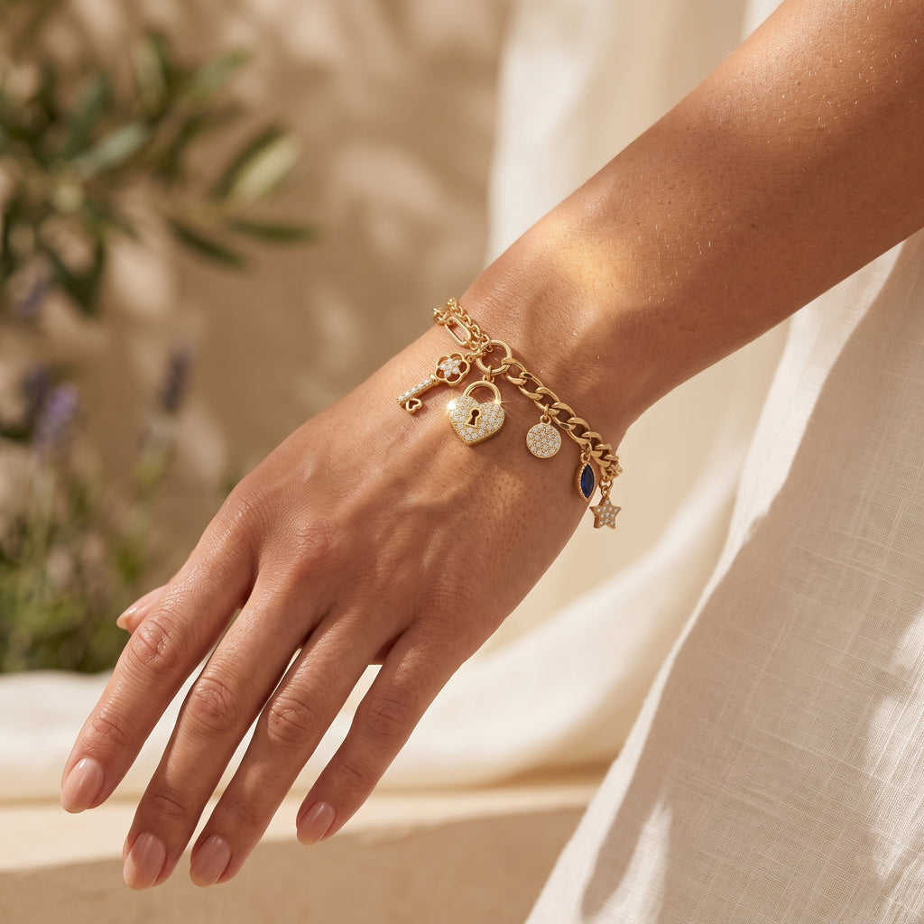 Close-up of a woman's wrist wearing a L'azurde gold charm bracelet (8.60g), illuminated by warm summer sunlight against soft ivory linen. لقطة قريبة لمعصم امرأة ترتدي سوار تعليقات ذهبي من لازوردي (8.60 غرام)، تضيئها أشعة شمس الصيف الدافئة على خلفية من الكتان العاجي الناعم.