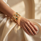 Close-up of a L'azurde 18k yellow gold bracelet worn on a woman's relaxed wrist resting on elegant draped ivory silk. لقطة مقربة لسوار من ذهب لازوردي الأصفر عيار 18 على معصم امرأة مسترخٍ يستند على قماش حرير عاجي أنيق ومنسدل.