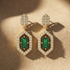 Gold earrings with green gemstones on a beige fabric background
