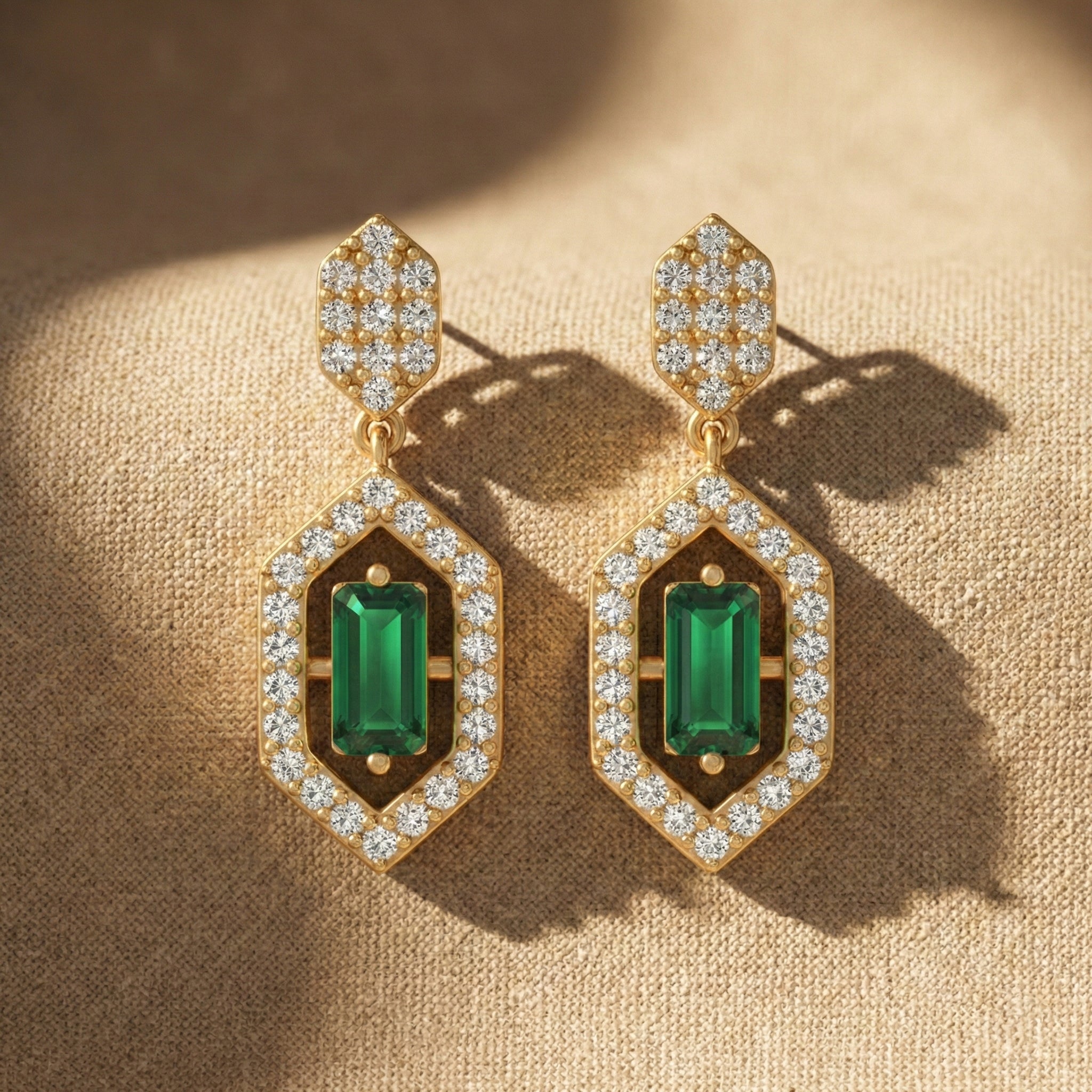 Gold earrings with green gemstones on a beige fabric background