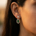 Close-up of an ear wearing a green gemstone earring with a blurred background