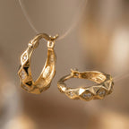 Gold hoop earrings with geometric design on a blurred background