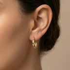 Close-up of an ear wearing a gold earring with a neutral background