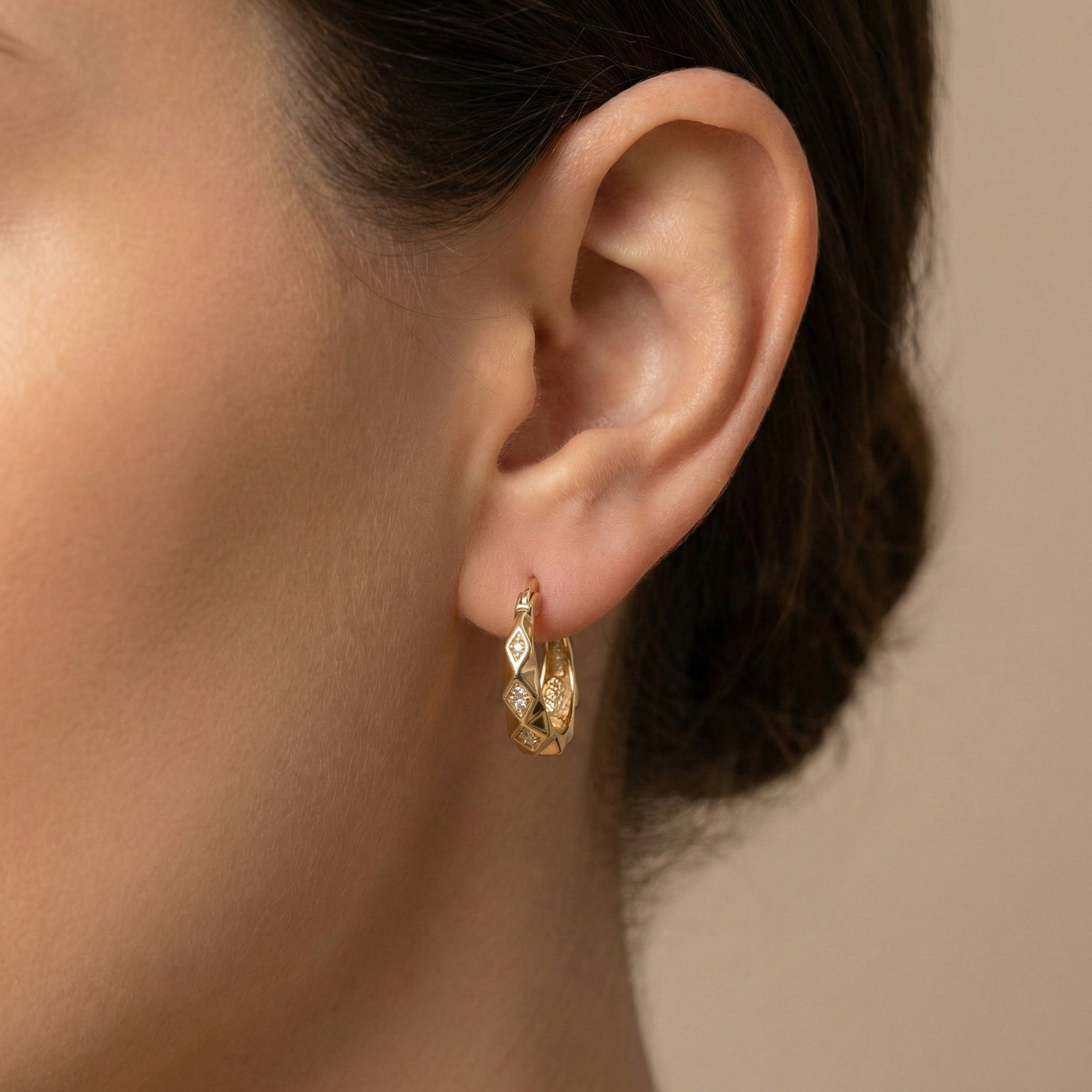 Close-up of an ear wearing a gold earring with a neutral background