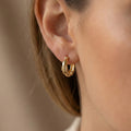 Gold hoop earrings worn by a person with a neutral background