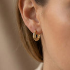 Gold hoop earrings worn by a person with a neutral background