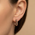 Close-up of an ear wearing a rose gold hoop earring on a beige background