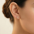 Close-up of an ear wearing a gold and diamond earring on a neutral background