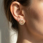 Close-up of an ear wearing a gold and pearl earring against a neutral background