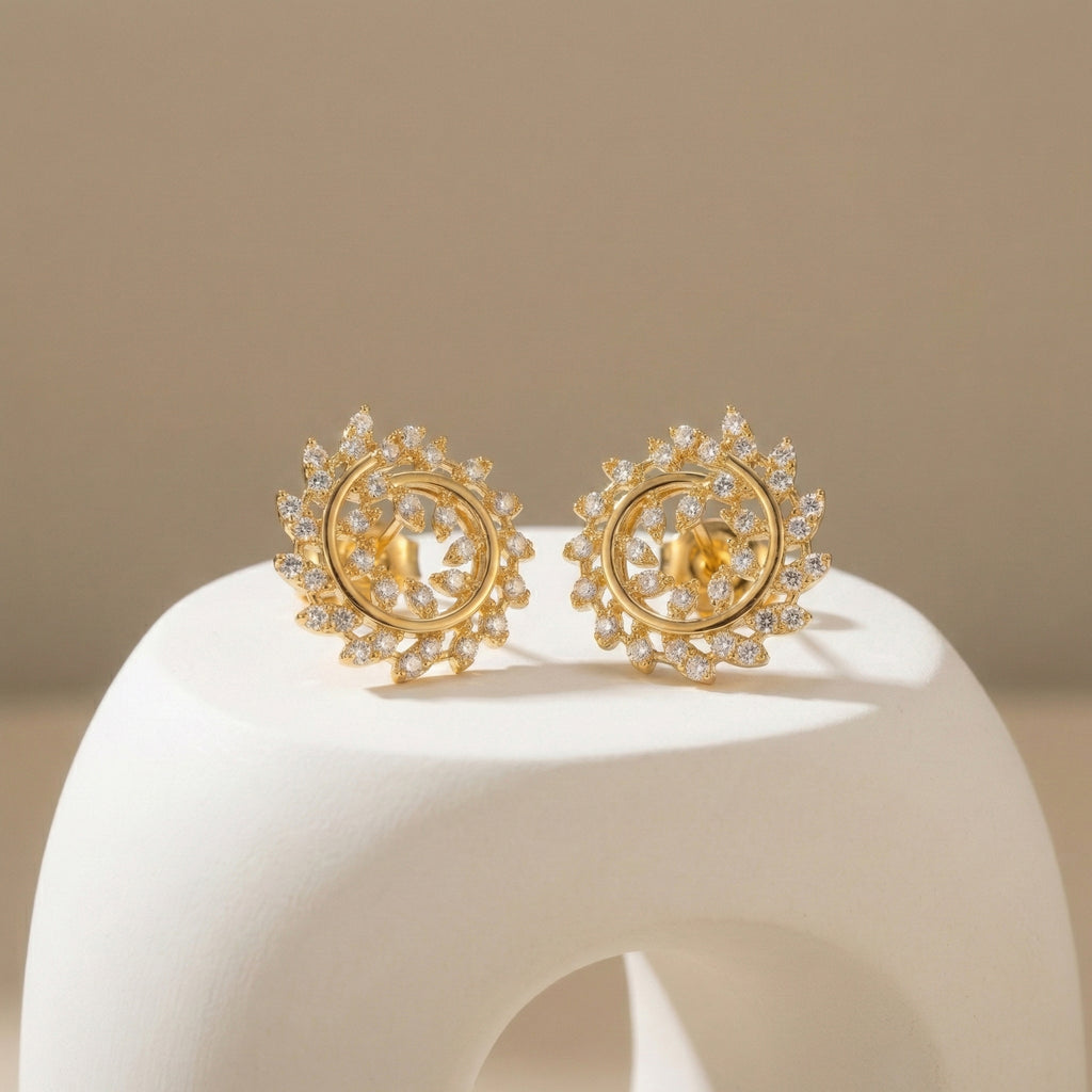 Pair of gold earrings with intricate designs on a beige background