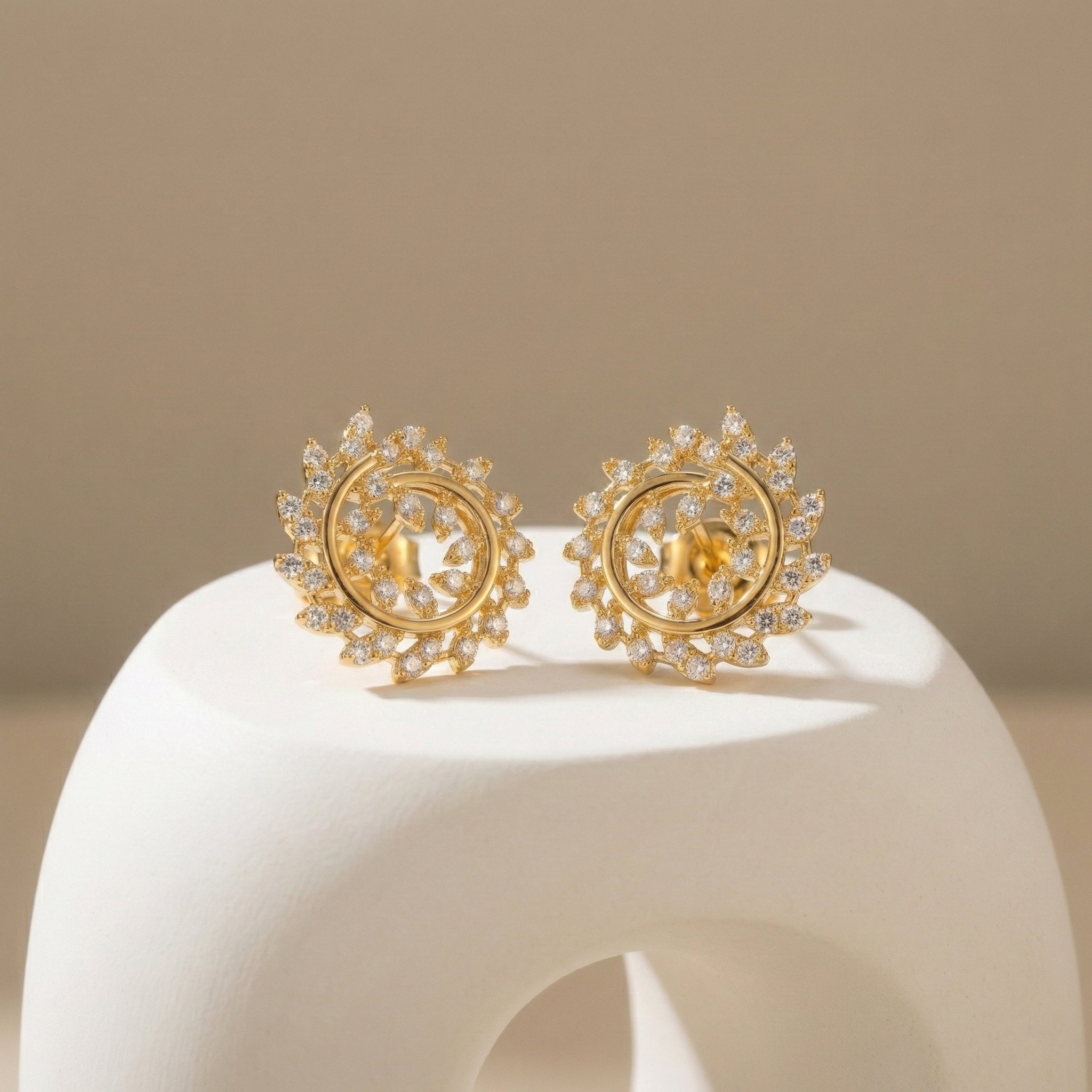 Pair of gold earrings with intricate designs on a beige background