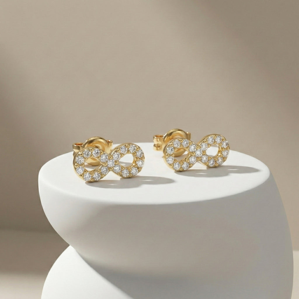 Gold earrings with diamond accents on a white pedestal against a beige background
