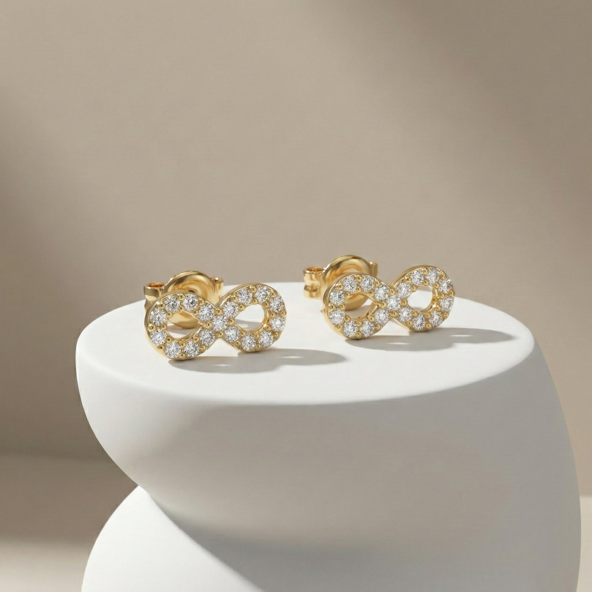 Gold earrings with diamond accents on a white pedestal against a beige background