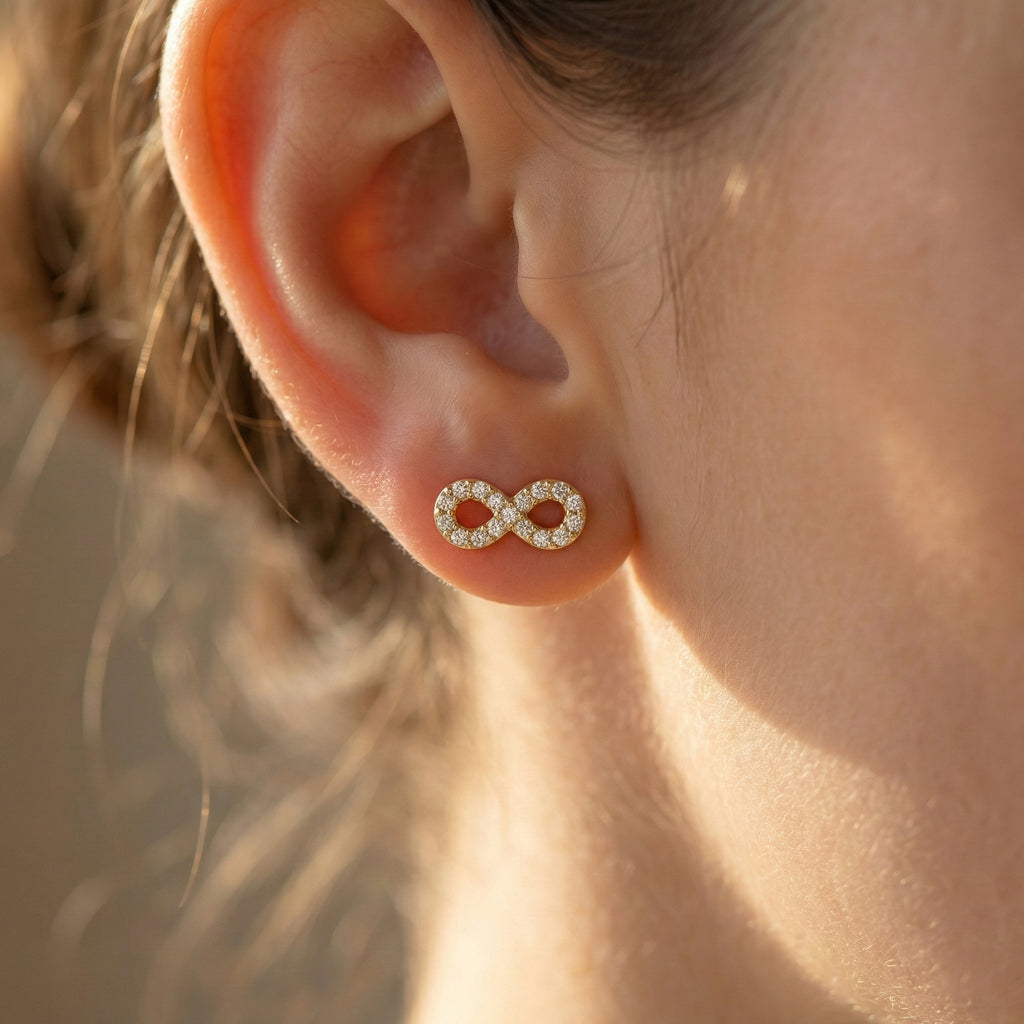 Close-up of an ear wearing a gold infinity symbol earring with a blurred background