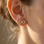 Close-up of an ear wearing a gold infinity symbol earring with a blurred background