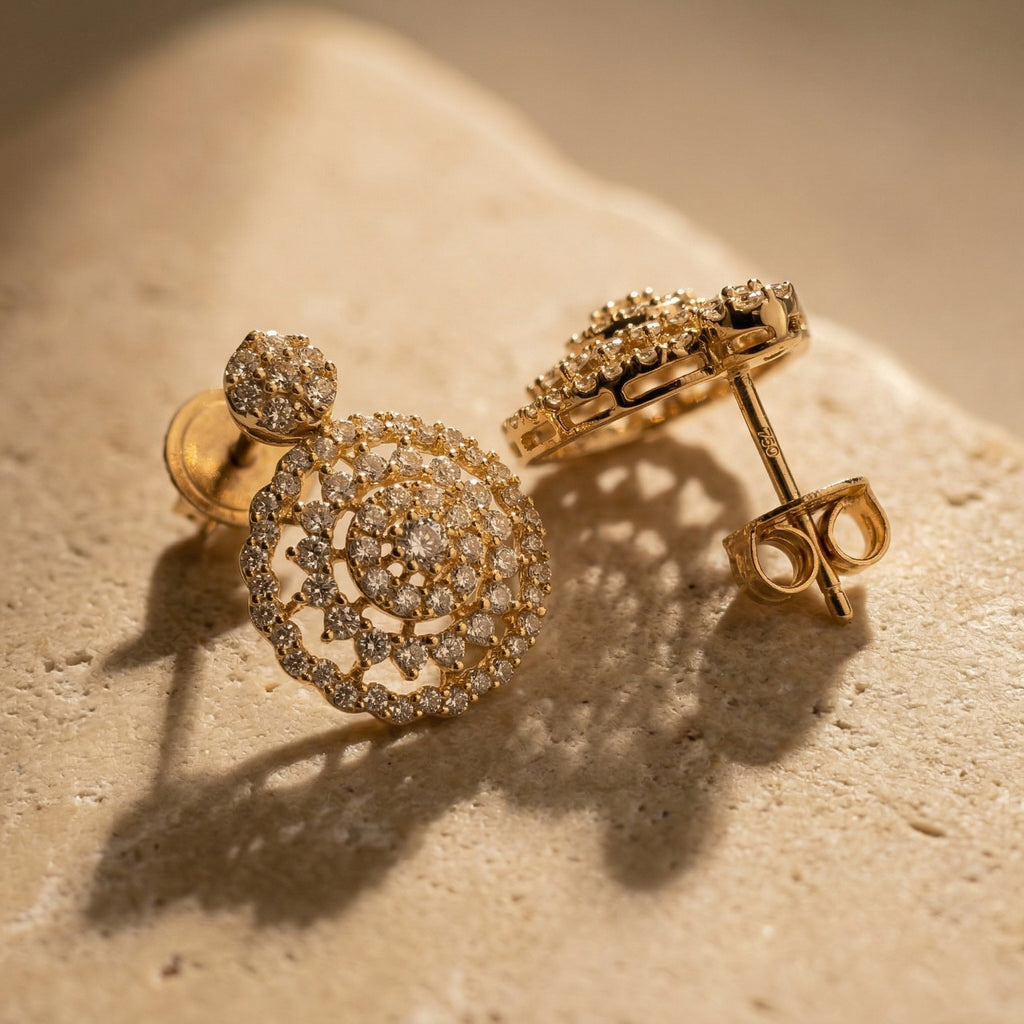 A luxury close-up of Lazurde 18k yellow gold earrings resting on a textured, neutral stone surface, featuring soft, artistic shadows that highlight the pristine gold craftsmanship and glittering stone details.