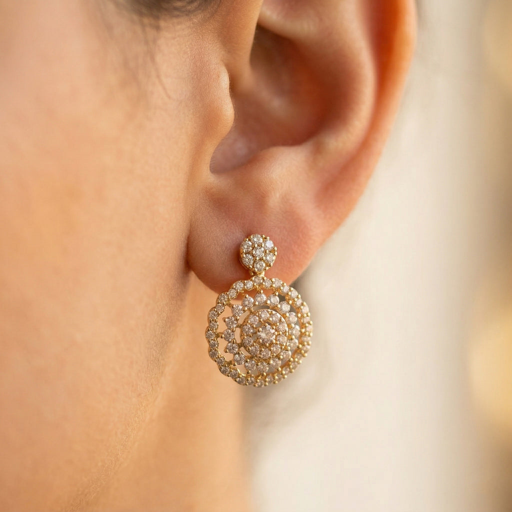 A warm, softly lit luxury profile photo of a person wearing a Lazurde 18k yellow gold earring, showcasing the intricate, stone-encrusted circular design resting elegantly on the ear against a blurred background.