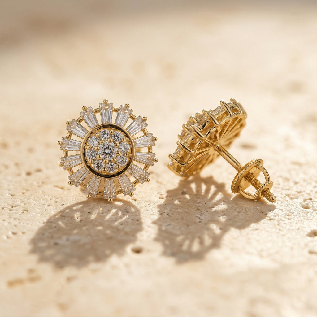 A high-end close-up of Lazurde 18k yellow gold earrings resting on a neutral, textured stone surface. Warm sunlight casts soft, artistic shadows that emphasize the meticulous craftsmanship and striking baguette-cut halo.
