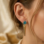 Side profile of a woman wearing Lazurde 18k yellow gold spike earrings with a trillion-cut teal gemstone, captured in soft warm lighting with a shallow depth of field for a luxury look.