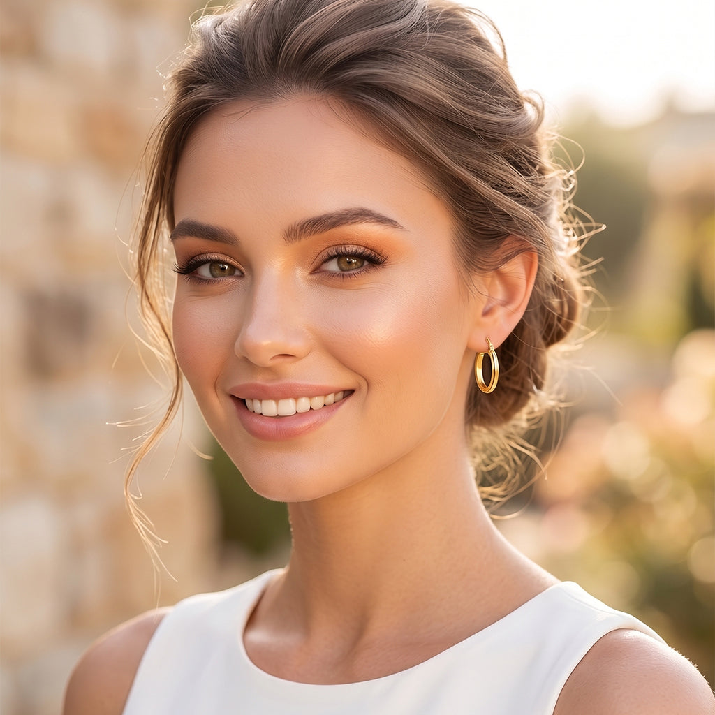 Elegant smiling woman outdoors wearing only 18k yellow gold elongated oval-grooved hoop earrings.