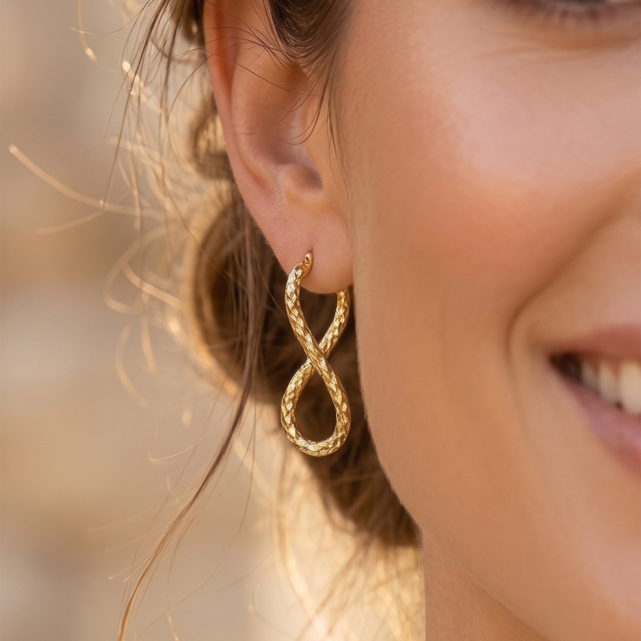 Extreme close-up of a textured UNO brand 18k yellow gold infinity hoop earring worn by a smiling model.
تصوير ماكرو قريب لحلق أونو دهب عيار 18 بتصميم إنفينيتي منقوش على موديل مبتسمة