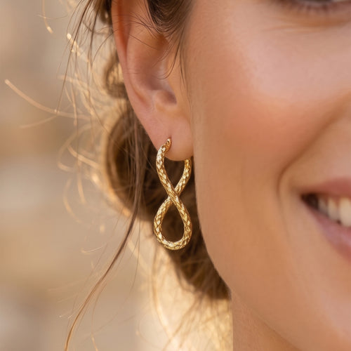 Extreme close-up of a textured UNO brand 18k yellow gold infinity hoop earring worn by a smiling model.
تصوير ماكرو قريب لحلق أونو دهب عيار 18 بتصميم إنفينيتي منقوش على موديل مبتسمة